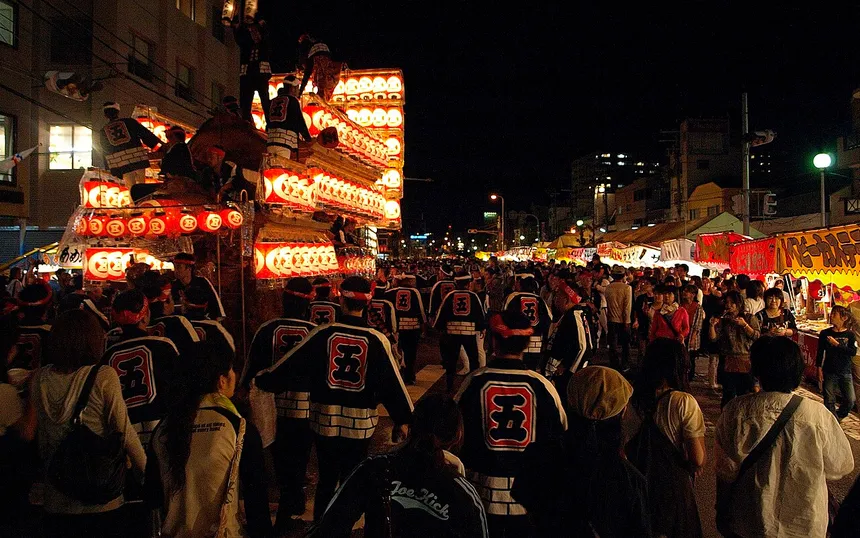 A danjiri hung with paper lanterns moving through the evening crowd in Kishiwada; photographed at the September festival
