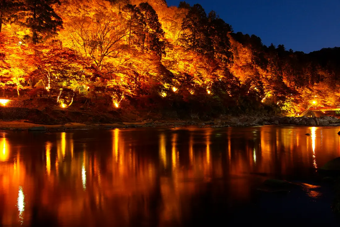 The illuminated maple hillside of Korankei reflected in the Tomoe river